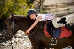 A little girl hugging a horse that she is riding.