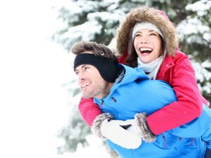 A happy woman getting a piggyback ride from her boyfriend in a winter forest.