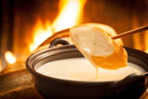A piece of bread being dipped in tasty cheese fondue in front of a fire.