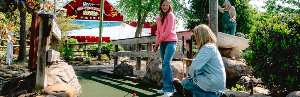 Two women are playing golf at Ripley’s Old MacDonald’s Farm Mini Golf