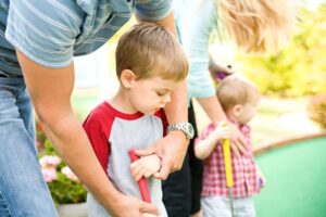 Parents teaching kids how to play mini golf.