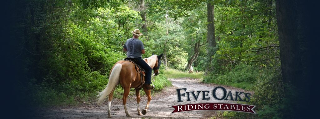 Man in a hat is riding a horse at Five Oaks Riding Stables